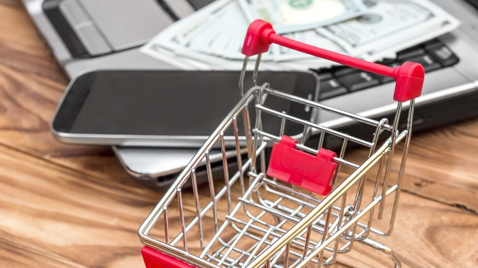 Shopping cart and laptop with money and smartphone on the table. Online shopping and Ecommerce.