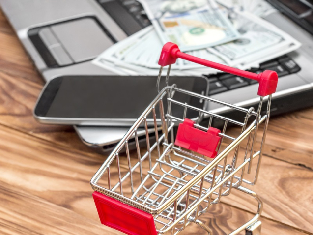 Shopping cart and laptop with money and smartphone on the table. Online shopping and Ecommerce.